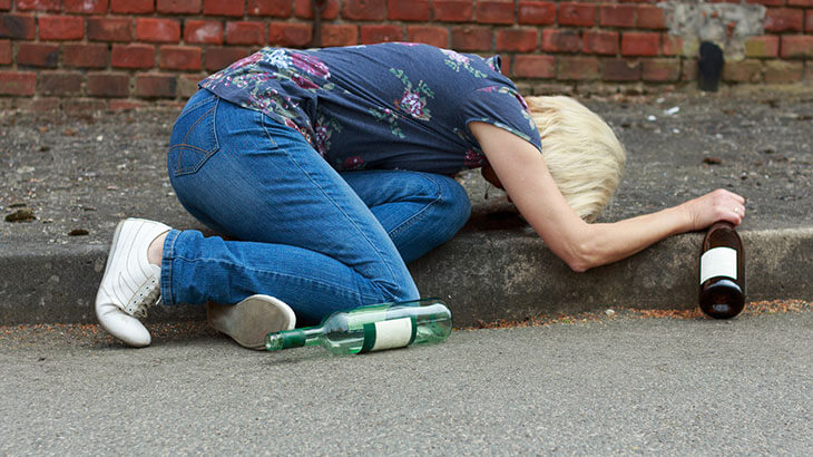 Женщина заболела алкоголизмом, пьяная лежит возле тротуара.