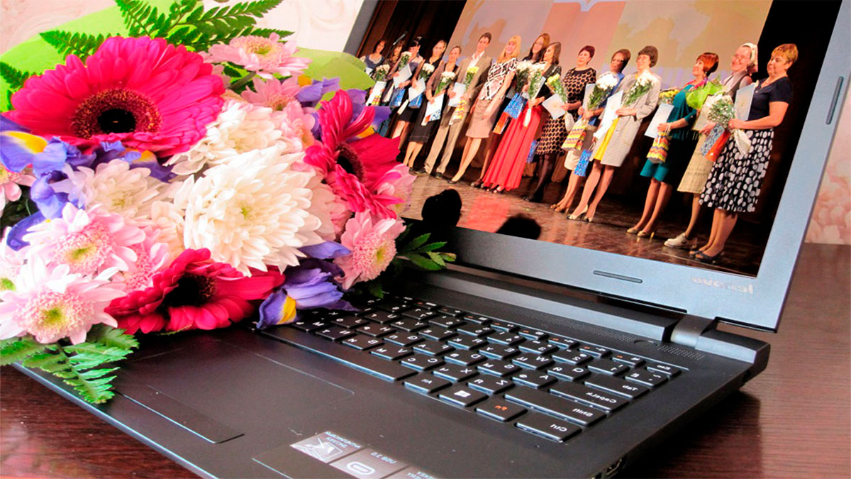 На столе лежит открытый ноутбук, на одной его половине лежат красивые цветы